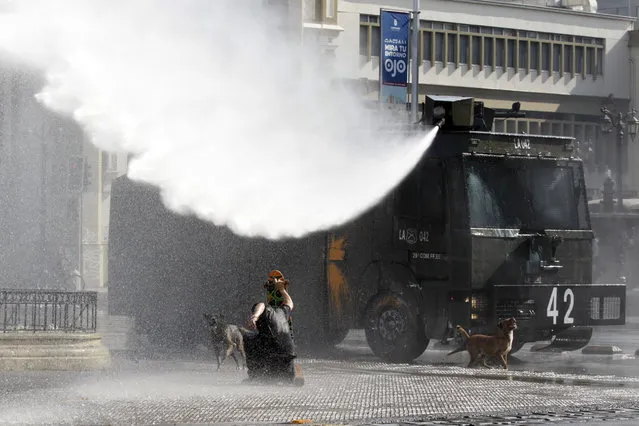 A protester confronts a jet of water shot from a police operated water cannon, during a student protest, in Santiago, Chile, Thursday, May 14, 2015. (Photo by Luis Hidalgo/AP Photo)