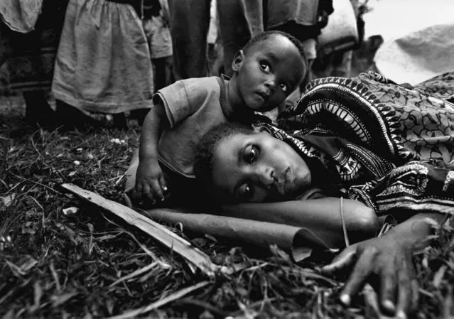 A baby sits next to his mother, who became gravely ill during their journey from Gisenyi, Rwanda, to Kigali, the capital; 1996. (Photo by Carol Guzy/The Washington Post)