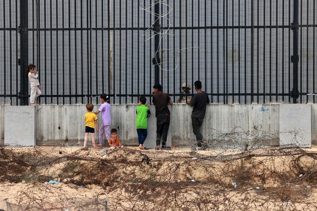 Displaced Palestinian children chat with an Egyptian soldier standing guard behind the fence between Egypt and Rafah in the southern Gaza Strip on April 26, 2024, amid the ongoing conflict between Israel and the Palestinian militant group Hamas. (Photo by Mohammed Abed/AFP Photo)