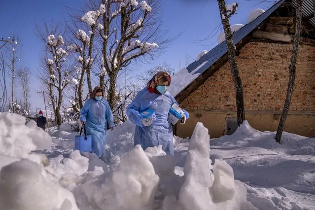 Fozia, right and Tasleema, Kashmiri healthcare workers, carry vaccines as they walk on a snow covered road during a COVID-19 vaccination drive in Budgam, southwest of Srinagar, Indian controlled Kashmir, January 11, 2022. (Photo by Dar Yasin/AP Photo)