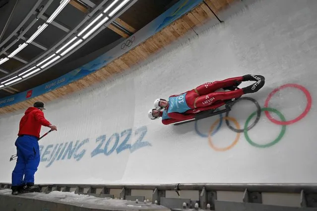 Latvia's Martins Bots and Roberts Plume take part in luge doubles training, as a track worker looks on, at the Yanqing National Sliding Centre during the Beijing 2022 Winter Olympic Games in Yanqing on February 6, 2022. (Photo by Daniel Mihailescu/AFP Photo)