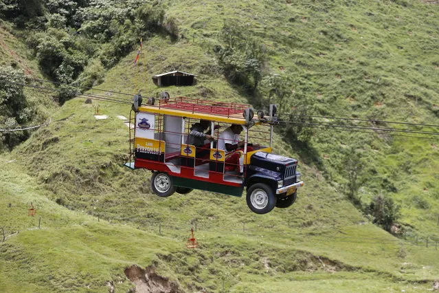 Tourists ride a cable car in the form a of a Chiva, a bus used to serve rural routes, in Pitalito, Colombia, Tuesday, April 5, 2017. The ride called “La Chiva Voladora” costs about $0.70 and you zip along fro about 800 meters from one side of a hill to another. (Photo by Fernando Vergara/AP Photo)