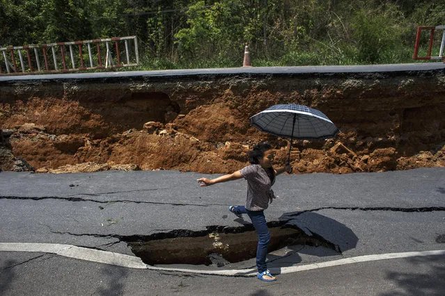 A woman with an umbrella jumps over a hole on a highway road, damaged by Monday's earthquake in Chiang Rai, in northern Thailand May 6, 2014. The earthquake of 6 magnitude struck northern Thailand on Monday causing some damage to buildings and roads and knocking goods off shelves in shops but there were no immediate reports of any casualties. The quake struck 17 miles (27 km) southwest of the town of Chiang Rai, the U.S. Geological Survey (USGS). It was felt in the Thai capital, Bangkok, and in neighbouring Myanmar. (Photo by Athit Perawongmetha/Reuters)