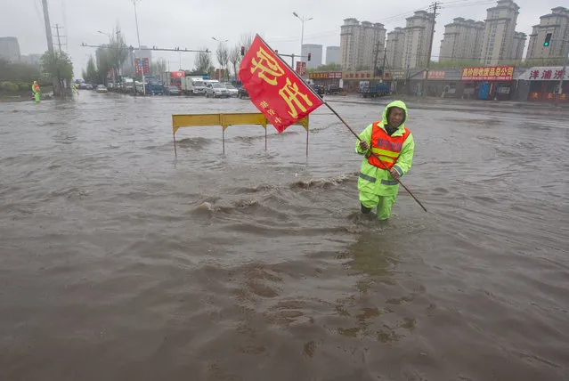 A man stands in water for hours as he waves a flag to warn drivers of an uncovered drain after a heavy rain in Changchun, Jilin Province, China, May 3, 2016. (Photo by Reuters/Stringer)