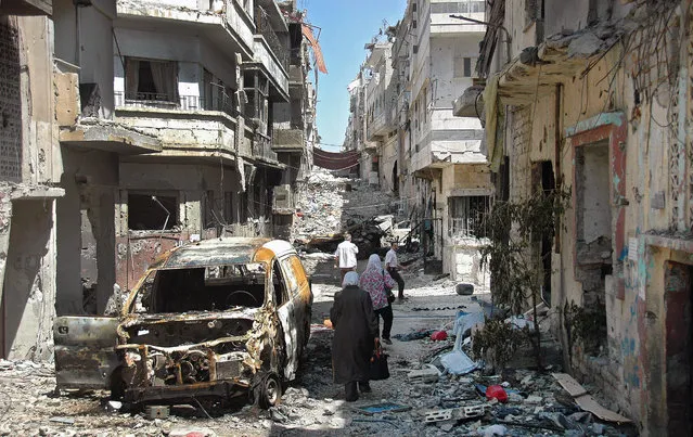 Syrian civilians carry their belongings walk next to damaged buildings as they return to inspect their homes in Jouret Al Chyah area, in Homs, Syria, May 10, 2014, after government troops entered the neighborhoods as part of an agreement that also granted fighters safe exit from the city on May 8. (Photo by EPA)