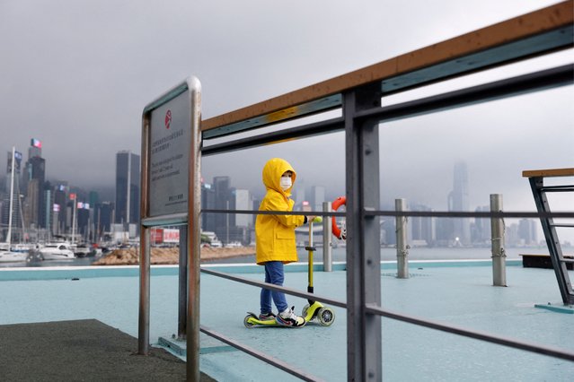 A child wearing a raincoat rides a scooter next to Victoria Harbour, amid the coronavirus disease (COVID-19) pandemic, in Hong Kong, China, March 25, 2022. (Photo by Tyrone Siu/Reuters)