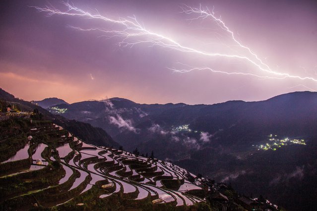 The photo taken on April 16, 2024 shows a bolt of lightning crossing the sky over the terraced fields in Congjiang, in China's southwestern Guizhou province. (Photo by AFP Photo/China Stringer Network)