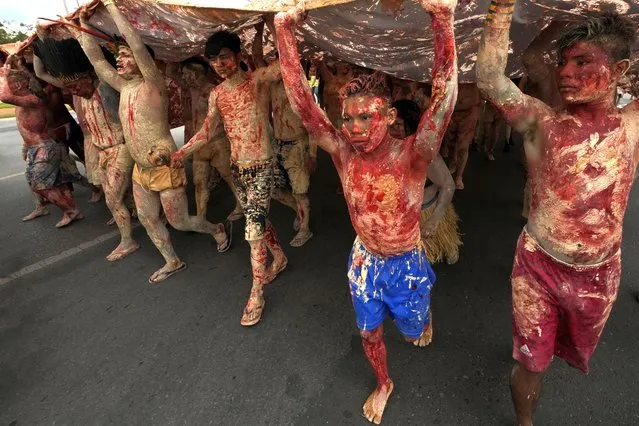 Indigenous people painted with red ink representing spilled Indigenous blood and clay representing gold, march during a protest against the increase of mining activities that are encroaching on their land, in front of the Ministry of Mines and Energy, in Brasilia, Brazil, Monday, April 11, 2022. (Photo by Eraldo Peres/AP Photo)
