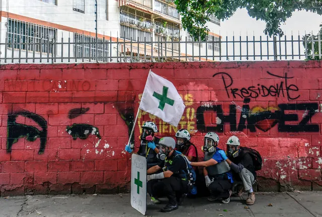 Medical staff seek shelter, during clashes between opposition activists and riot police, in a protest against President Nicolas Maduro's government in Caracas on June 3, 2017. Venezuela's President Nicolas Maduro has offered to hold a referendum on contested constitutional reforms in an apparent bid to calm critics in his own camp as he resists opposition efforts to remove him from office. The surprise announcement late Thursday followed two months of deadly unrest during anti-government protests and signs of division in the socialist leader's side. (Photo by  Juan Barreto/AFP Photo)
