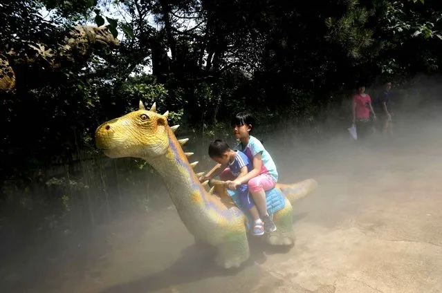 A couple watches children riding on a battery-powered electric dinosaur vehicle on International Children's Day at a dinosaur park inside the Shijingshan Amusement Park in Beijing, Wednesday, June 1, 2016. (Photo by Andy Wong/AP Photo)