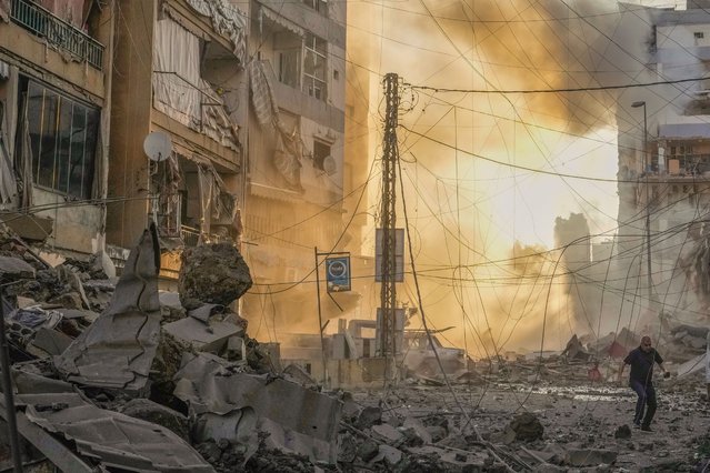 A man runs for cover as a smoke raises in the background following an Israeli airstrike in Dahiyeh, Beirut, Lebanon, Friday, October 4, 2024. (Photo by Hassan Ammar/AP Photo)