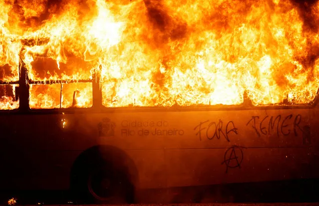 A bus burns during clashes between demonstrators and riot police in a protest against President Michel Temer's proposal reform of Brazil's social security system during general strike in Rio de Janeiro, Brazil, April 28, 2017. The writing reads, “Out Temer”. (Photo by Ricardo Moraes/Reuters)
