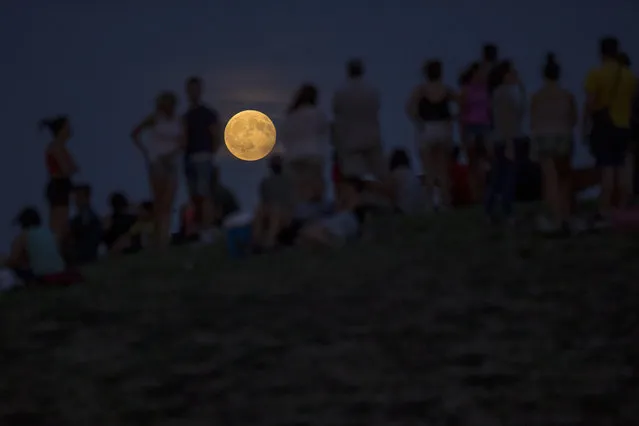 People watch at a rising full moon during a partial lunar eclipse atop a hill at the Tio Pio park in Madrid, Monday, August 7, 2017. (Photo by Francisco Seco/AP Photo)