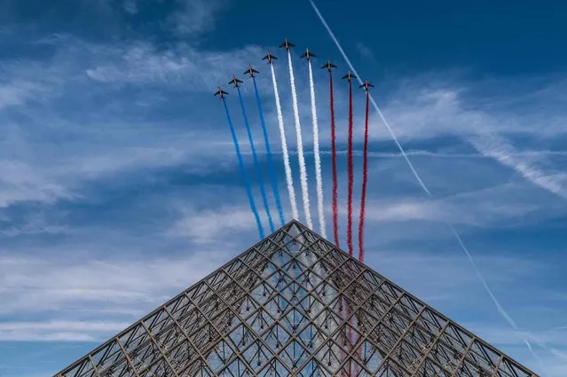 French elite acrobatic flying team “Patrouille de France” (PAF) release smoke in the colours of the French flag as they perform a fly-over the Louvre Pyramid during the Bastille Day military parade in Paris on July 14, 2022. (Photo by Martin Bureau/AFP Photo)