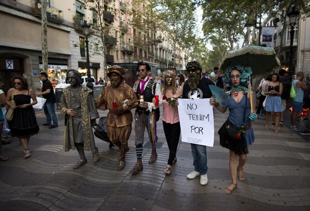 People dressed in costumes, one of them holding a banner reading in Catalan “we don't fear”, walk along Las Ramblas promenade after a van attack that killed at least 13, in central Barcelona, Spain, Friday, August 18, 2017. Police on Friday shot and killed five people carrying bomb belts who were connected to the Barcelona van attack, as the manhunt intensified for the perpetrators of Europe's latest rampage claimed by the Islamic State group. (Photo by Emilio Morenatti/AP Photo)