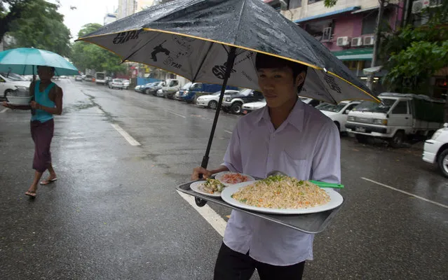 Two delivery men carry plates of food to customers across a street in the rain on July 8, 2016. Myanmar's rainy season generally lasts from June to September. (Photo by Romeo Gacad/AFP Photo)
