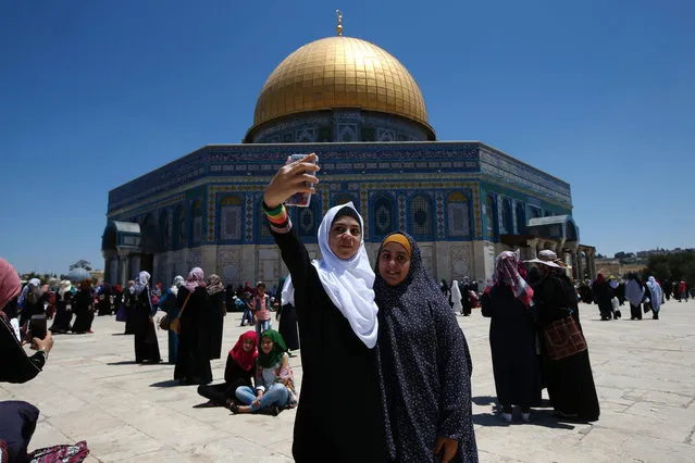Palestinian young women use a phone to take a selfie in front of the Dome of the Rock in Jerusalem's Al-Aqsa mosque compound during the last Friday prayers of the holy Muslim fasting month of Ramadan on July 1, 2016. (Photo by Ahmad Gharabli/AFP Photo)