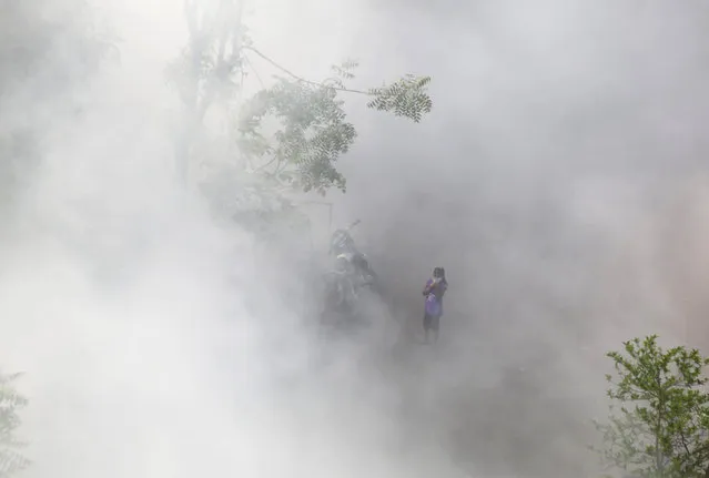 An Indian girl stands amid smoke as municipal workers fumigate an area spray disinfectants as a precautionary measure against COVID-19 in Ahmedabad, India, Sunday, March 29, 2020. Indian Prime Minister Narendra Modi apologized to the public on Sunday for imposing a three-week national lockdown, calling it harsh but “needed to win” the battle against the coronavirus pandemic. (Photo by Ajit Solanki/AP Photo)