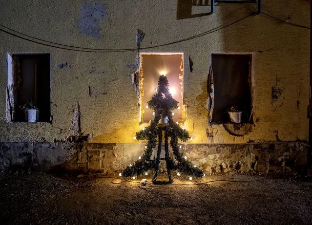 An illuminated Christmas tree leans against the window of a damaged house in Mayschoss in the Ahrtal valley, southern Germany, Tuesday, December 14, 2021. The region was hit by floodings exactly five months ago, causing the death of about 180 people. Amid the mud and debris still clogging the streets from last summer's devastating floods, residents of the Ahr Valley in western Germany are trying to spark some festive cheer with Christmas trees. (Photo by Michael Probst/AP Photo)
