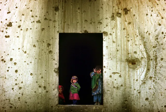 Afghan refugee children look from the window of their shelter in the former Soviet embassy, a huge compound amid the destruction of west Kabul, November 27, 2001. (Photo by Damir Sagolj/Reuters)