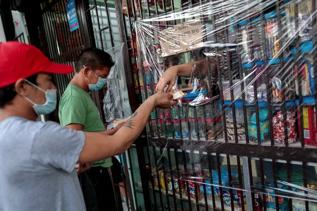 Customers wearing protective face masks make their transactions through a plastic barrier as a preventive measure against the coronavirus disease (COVID-19) in a local grocery in Quezon City, Metro Manila, Philippines on March 26, 2020. (Photo by Eloisa Lopez/Reuters)