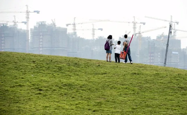 A family stands on an artificial grassland near a construction site of a residential complex, in Hefei, Anhui province, China, in this May 23, 2015 file photo. Angry Chinese authorities have seized up to 1 trillion yuan ($157 billion) from local governments who failed to spend their budget allocations, sources said, as Beijing seeks ways to stimulate economic growth which is at its slowest for 25 years. (Photo by Reuters/Stringer)