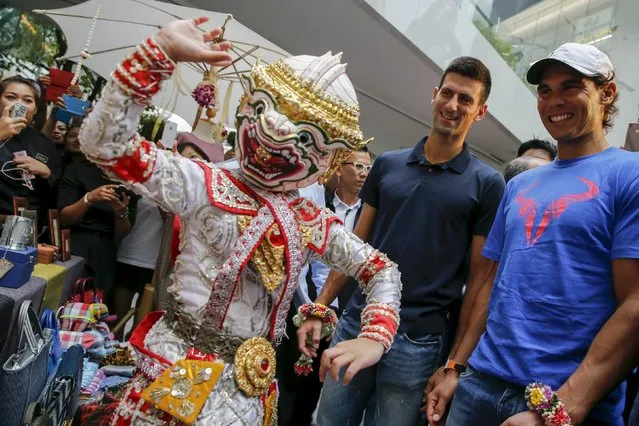 Tennis players Novak Djokovic of Serbia and Rafael Nadal of Spain (R) look at a Thai folklore dancer as they visit a handicraft market before their "Back To Thailand - Nadal vs Djokovic" friendly match on Friday, in Bangkok, Thailand, October 1, 2015. (Photo by Jorge Silva/Reuters)