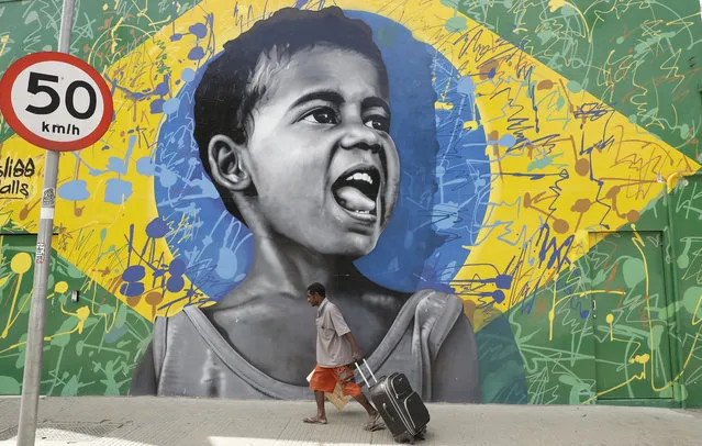 In this December 5, 2017 photo, a man walks past a wall mural depicting a child superimposed on a representation of the Brazilian national flag, in Sao Paulo, Brazil. After suffering through the deepest recession in its modern history, the largest corruption scandal in Latin America and a year under a deeply unpopular president, Brazilians are deeply frustrated and some are looking to extreme solutions. (Photo by Andre Penner/AP Photo)
