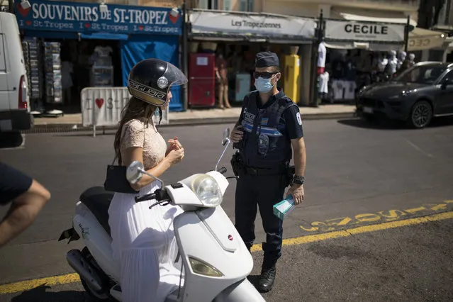 A police officer informs a woman about the mandatory face mask requirement in Saint-Tropez, southern France, Saturday August 8, 2020. The glamorous French Riviera resort of Saint-Tropez is requiring face masks outdoors starting Saturday, threatening to sober the mood in a place renowned for high-end, free-wheeling summer beach parties. (Photo by Daniel Cole/AP Photo)