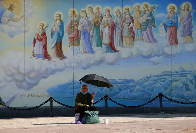 A woman sits under an umbrella and begs for money during a sunny day in front of the St. Michael's Golden-Domed Cathedral in Kyiv, Ukraine on July 22, 2020. (Photo by Gleb Garanich/Reuters)