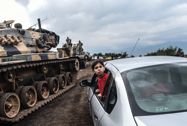 A Turkish girl leans out of a car window to have a look as Turkish army tanks and soldiers gather close to the Syrian border  at Hassa, in Hatay province on January 21, 2018. Turkish forces on January 20, 2018, began a major new operation aimed at ousting the Peoples' Protection Units (YPG) Kurdish militia from Afrin, pounding dozens of targets from the sky in air raids and with artillery. Turkey accuses the YPG of being the Syrian offshoot of the Kurdistan Workers' Party (PKK) which has waged a rebellion in the Turkish southeast for more than three decades and is regarded as a terror group by Ankara and its Western allies. (Photo by Bulent Kilic/AFP Photo)