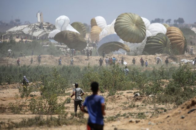 Palestinians rush to the site where parachuted aid packages are landing in the Nuseirat area in the central Gaza Strip during an airdrop above the Israel-besieged Palestinian territory on August 6, 2025. (Photo by Eyad Baba/AFP Photo)