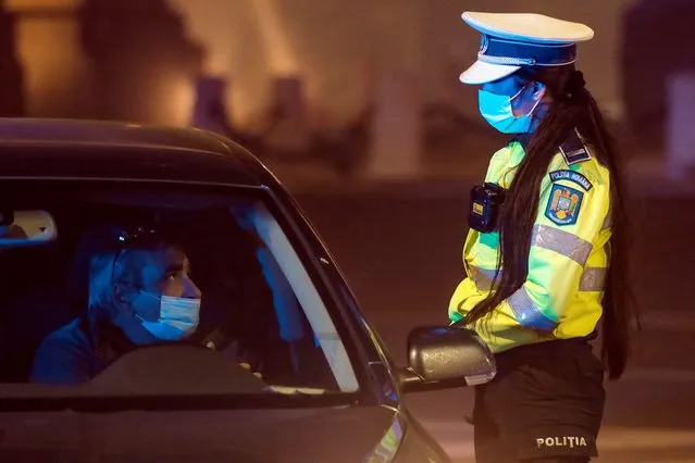 A police officer speaks to a driver shortly after midnight in Bucharest, Romania, Monday, November 9, 2020 informing him of the pandemic related night traffic restrictions that just came into effect. Romania introduces new restrictions aimed at limiting the spread of the COVID-19 infections following a week when it registered an all time high number of new infections. (Photo by Vadim Ghirda/AP Photo)