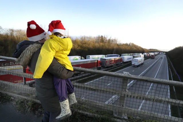 A mother and child look at the line of trucks parked up on the M20, part of Operation Stack in Ashford, Kent, England, Friday, December 25, 2020. Thousands wait to resume their journey across The Channel after the borders with France reopened. Trucks inched slowly past checkpoints in Dover and headed across the Channel to Calais on Thursday after France partially reopened its borders following a scare over a rapidly spreading new virus variant. (Photo by Kirsty Wigglesworth/AP Photo)