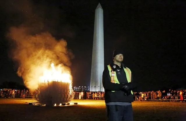 A fire safety worker watches a crowd of spectators and participants as an interactive art installation by artist Michael Verdon called the “Temple of Essence” and dedicated to "victims of the war on drugs" is burned on the U.S. National Mall in front of the Washington Monument in Washington November 22, 2015. (Photo by Jim Bourg/Reuters)
