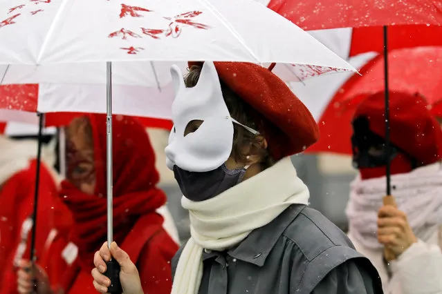 Women wearing carnival masks march down the streets under umbrellas with colors of the former white-red-white flag of Belarus to protest against the Belarus presidential election results in Minsk, on January 26, 2021. (Photo by AFP Photo/Stringer)