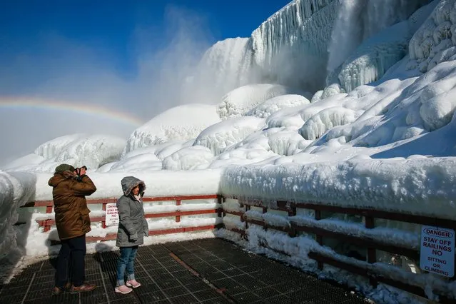 Visitors view water flowing around ice at the base of the American Falls due to cold temperatures in Niagara Falls, New York, U.S., February 21, 2021. (Photo by Lindsay DeDario/Reuters)
