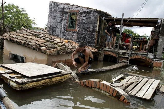 A man works near houses that are partially submerged in flood waters in Asuncion, December 20, 2015. The National Emergency Secretary estimates that about 65,000 people are affected by the flooding of the country's two main rivers, the Paraguay and the Parana. (Photo by Jorge Adorno/Reuters)