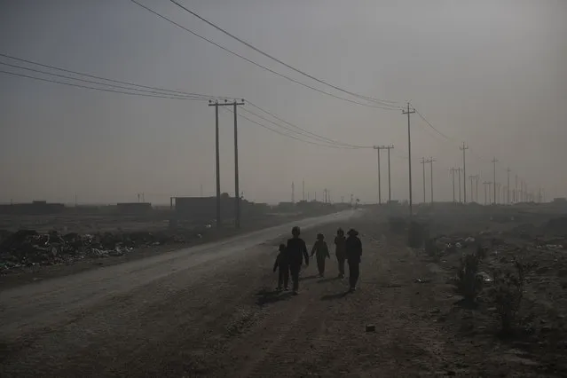 Children walk among smoke from burning oil fields in Qayara, south of Mosul, Iraq, Tuesday, November 22, 2016. (Photo by Felipe Dana/AP Photo)