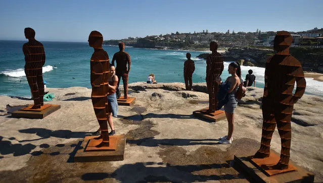 Visitors pose with sculptures titled Shifting Horizons by artist April Pine, part of the annual Sculpture by the Sea exhibiton in Sydney on October 19, 2018. The annual event showcases artists from all over the world exhibited on the coastal walk between Bondi Beach and Tamarama. (Photo by Peter Parks/AFP Photo)