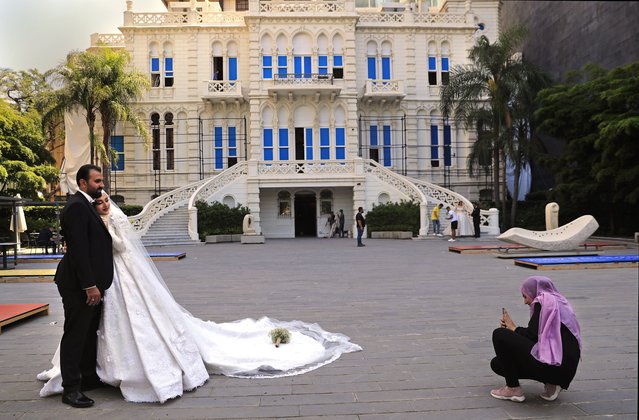 A woman takes pictures of a Lebanese bride and groom in the courtyard of the Sursock Museum, which was damaged in the explosion last August at Beirut's port, in Beirut, Lebanon on July 27, 2021. (Photo by Hussein Malla/AP Photo)