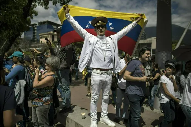 Jose Ramon Salas strikes a pose holding a Venezuelan national flag and wearing a Russian military cap at an opposition rally to propose amnesty laws for police and military, in Las Mercedes neighborhood of Caracas, Venezuela, Saturday, January 26, 2019. “If the Berlin Wall can fall, why not Maduro and his government?!” (Photo by Rodrigo Abd/AP Photo)