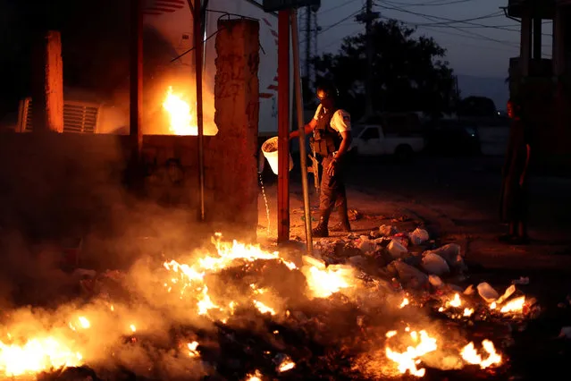 A policeman tries to put out burning garbage used to block a street as part of anti-government protests in Port-au-Prince, February 18, 2019. (Photo by Ivan Alvarado/Reuters)