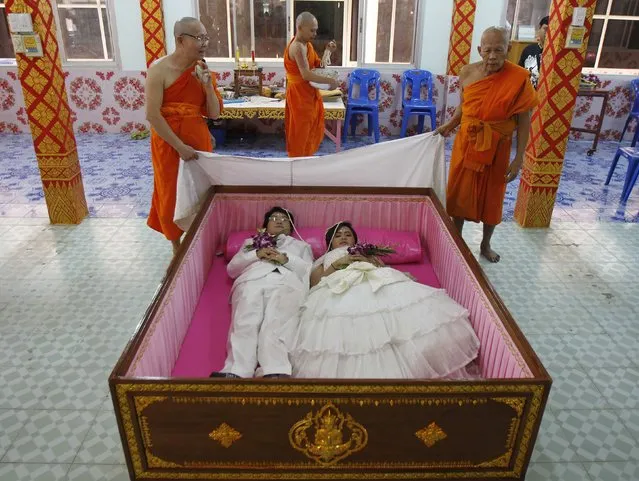 Groom Tanapatpurin Samangnitit (bottom L), 40, and his bride Sunantaluk Kongkoon, 26, lie in a coffin during a wedding ceremony at Wat Takien temple in Nonthaburi province, on the outskirts of Bangkok February 14, 2014. Seven Thai couples laid in the pink coffin on Friday during the wedding ceremony organised by the Buddhist temple on Valentine's Day. Couples believe laying briefly in the coffin will get rid of bad luck and usher happiness into their lives. (Photo by Chaiwat Subprasom/Reuters)