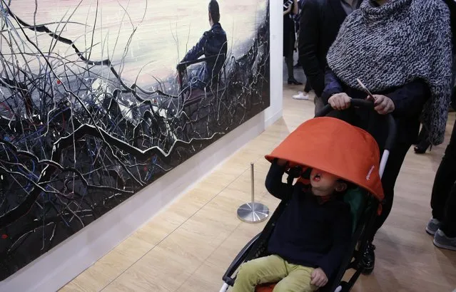 A boy sits in a stroller near a painting “Self-Portrait” created by Chinese artist Zeng Fanzhi during the VIP preview of the art fair “Art Basel” in Hong Kong, Tuesday, March 22, 2016. (Photo by Kin Cheung/AP Photo)