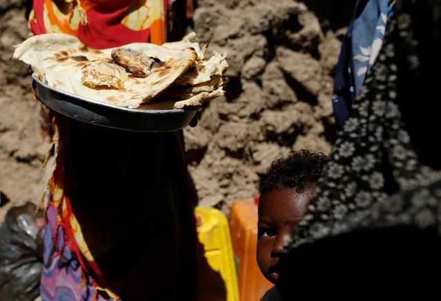 A boy looks as a woman holds bread she just made outside her hut at a makeshift camp for internally displaced people near Sanaa, Yemen January 28, 2019. (Photo by Khaled Abdullah/Reuters)