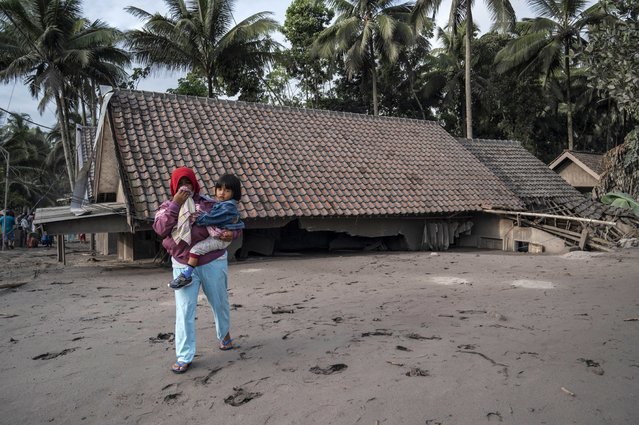 Villagers walk next to houses covered in volcanic ash at Sumber Wuluh village in Lumajang on December 5, 2021, after the Semeru volcano eruption that killed at least 13 people. (Photo by Juni Kriswanto/AFP Photo)