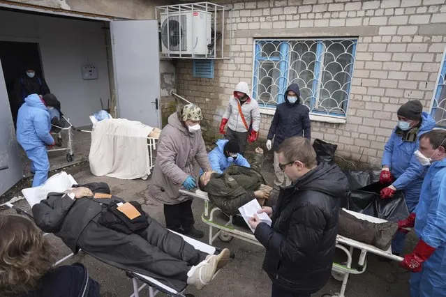 Dead bodies are prepared before being put into body bags and buried in a mass grave on the outskirts of Mariupol, Ukraine, Wednesday, March 9, 2022. (Photo by Evgeniy Maloletka/AP Photo)