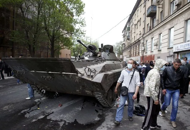 People pass by a broken armoured vehicle left behind after Ukrainian forces attacked police headquarters in an attempt to drive out pro-Russian militants in Mariupol May 9, 2014. (Photo by Marko Djurica/Reuters)