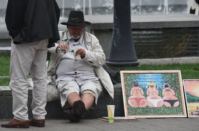 A street artist drinks vodka as he sells his paintings to tourists in the center of Ukrainian capital of Kiev, on August 16, 2019. (Photo by Sergei Supinsky/AFP Photo)